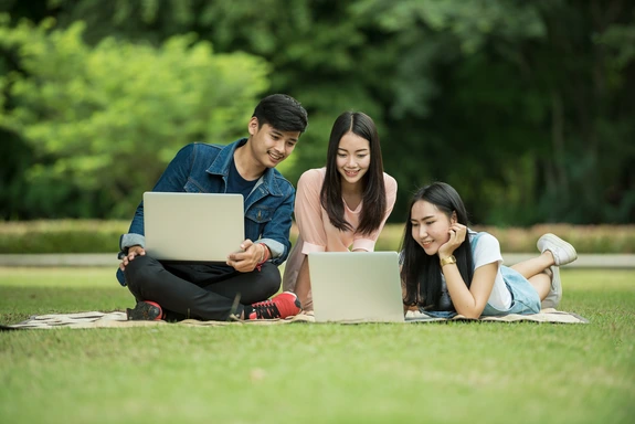 Students sitting in a field doing work on their laptops